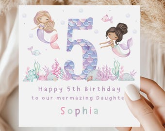 Puede incluir: Una tarjeta de cumpleaños con temática de sirena. La tarjeta presenta un número 5 morado con escamas de sirena, dos sirenas y el texto "Feliz 5º cumpleaños a nuestra hija mermazing Sophia".