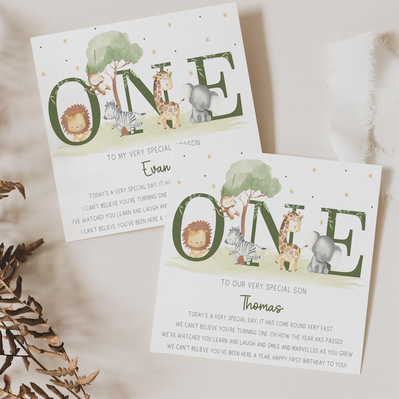 May include: Two green and white cards with the word "ONE" in large green letters. The letters are decorated with animal illustrations. The cards are personalized with the names "Evan" and "Thomas" and include a message about celebrating a first birthday.