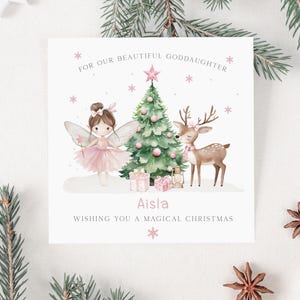 May include: A Christmas card with a fairy, deer, and Christmas tree illustration. The fairy wears a pink tutu and has wings. The deer has a pink scarf. The card reads "For our beautiful goddaughter" and "Wishing you a magical Christmas."