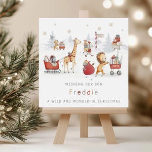 K&ouml;nnte beinhalten: Weihnachtskarte auf einer Holzstaffelei. Die Illustration zeigt Tiere, die Geschenke tragen. Der Text lautet: &bdquo;Wir w&uuml;nschen unserem Sohn Freddie ein wildes und wundervolles Weihnachtsfest.&ldquo;
