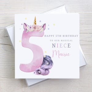 May include: A pink unicorn with a gold horn and purple flowers on its head. The unicorn is holding a pink number 5. The card says "Happy 5th Birthday to our magical niece Maisie".