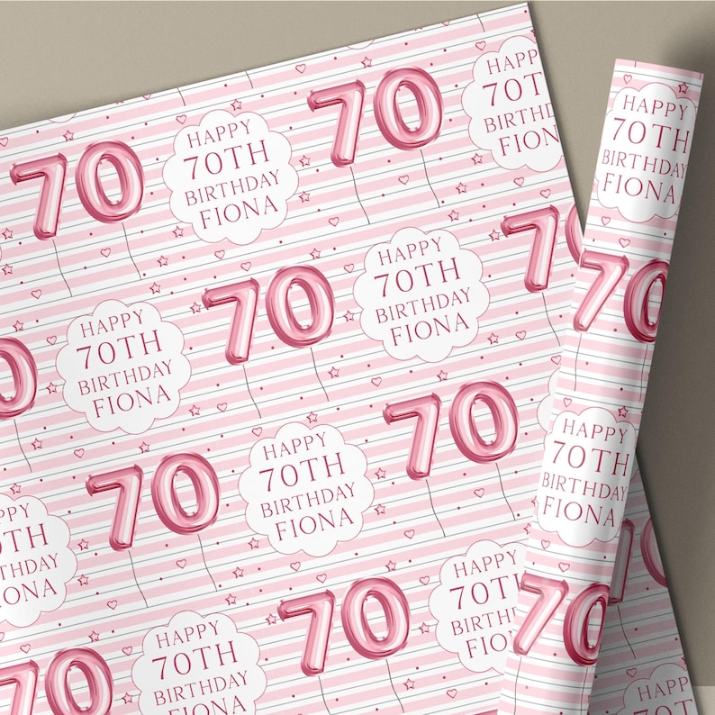May include: Pink wrapping paper with a repeating pattern of the number 70 in a balloon font, the text "Happy 70th Birthday Fiona", hearts, and stars. The background has pink and white stripes.
