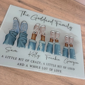 May include: A rectangular glass chopping board with the text "The Goddard Family." The image features illustrations of feet in jeans and trainers. The names Sam, Kelly, Frankie, and Georgia are printed below the illustrations, along with a quote.