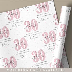May include: White wrapping paper with a pink floral pattern. The paper features the number 30 with the word "thirty" written in cursive. The text "Happy 30th Birthday to a Very Special Daughter" is repeated throughout the paper. The name "Olivia" is also repeated throughout the paper.