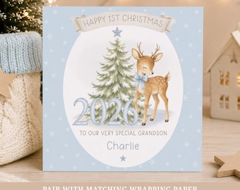May include: A square Christmas greeting card with a light blue background featuring white snowflakes. The center shows a green Christmas tree, a fawn with a blue bow, the text HAPPY 1ST CHRISTMAS, 2026, TO OUR VERY SPECIAL GRANDSON, and Charlie.