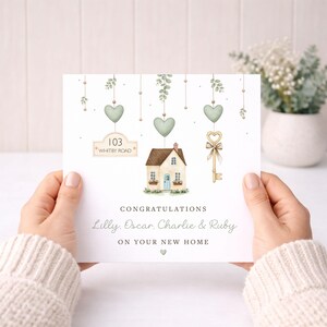 May include: A greeting card with a watercolor illustration of a house, key, and hanging hearts. The card reads "Congratulations Lilly, Oscar, Charlie & Ruby on your new home." The address "103 Whitby Road" is also displayed.