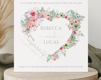 May include: A white card with a floral heart design and the text "TO A VERY SPECIAL DAUGHTER & FUTURE SON-IN-LAW" at the top. The heart is made of pink and green flowers and leaves. Inside the heart, the text reads "REBECCA and LUCAS congratulations on your engagement HERE'S TO THE BEGINNING OF YOUR HAPPILY EVER AFTER".