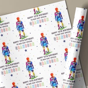 May include: White wrapping paper featuring a repeating pattern of a soccer player in a blue and orange uniform. The text reads "Happy 12th Birthday! To our very special Grandson" with colorful stars.