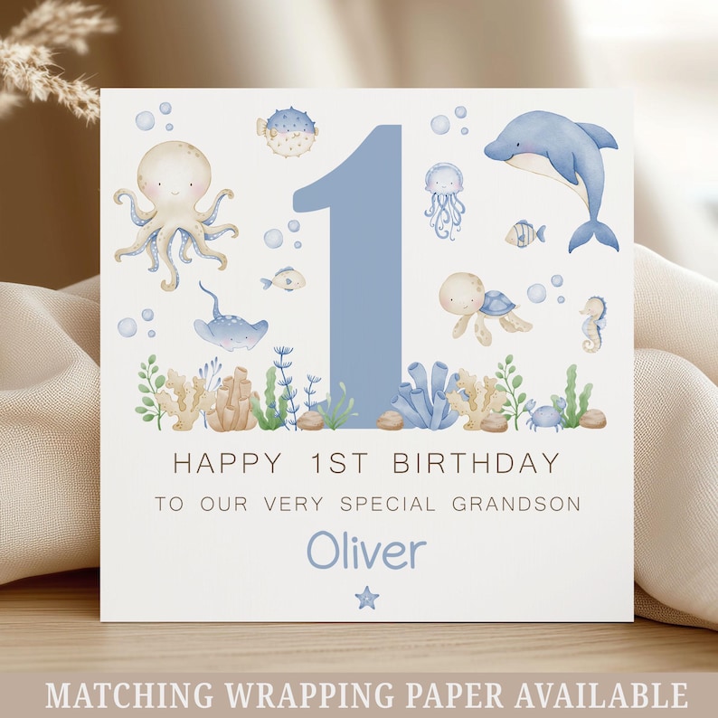 Puede incluir: Tarjeta de felicitaci&oacute;n cuadrada con un n&uacute;mero 1 azul y ilustraciones marinas, incluyendo un pulpo, un delf&iacute;n y una tortuga. El texto dice: "Feliz 1er cumplea&ntilde;os a nuestro nieto muy especial Oliver."