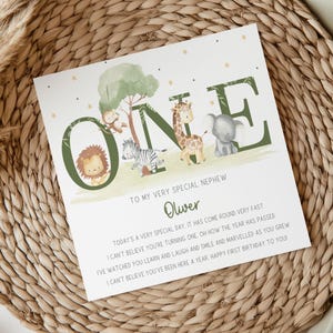 May include: A green and white card with the word "ONE" in large green letters. The letters are decorated with animal illustrations, including a giraffe, zebra, elephant, and lion. The card has a message for a nephew, "To my very special nephew Oliver. Today's a very special day. It has come round very fast. I can't believe you're turning one. Oh how the year has passed. I've watched you learn and laugh and smile and marvelled as you grew. I can't believe you've been here a year, happy first birthday to you!"