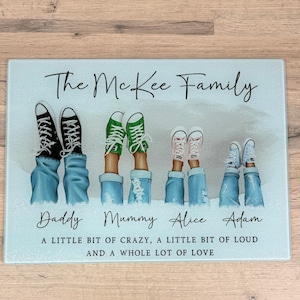 May include: A rectangular glass chopping board featuring the text "The McKee Family." The image shows five pairs of legs in jeans and trainers: black, green, pink, and white. The names "Daddy," "Mummy," "Alice," and "Adam" are below the legs. The text "A LITTLE BIT OF CRAZY, A LITTLE BIT OF LOUD AND A WHOLE LOT OF LOVE" is at the bottom.