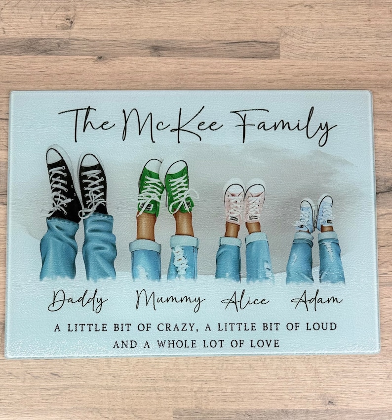 May include: A rectangular glass chopping board featuring the text "The McKee Family." The image shows five pairs of legs in jeans and trainers: black, green, pink, and white. The names "Daddy," "Mummy," "Alice," and "Adam" are below the legs. The text "A LITTLE BIT OF CRAZY, A LITTLE BIT OF LOUD AND A WHOLE LOT OF LOVE" is at the bottom.