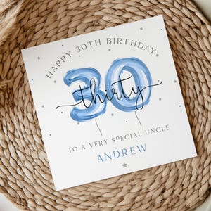 May include: A white card with blue and silver foil accents. The card says "Happy 30th Birthday" with a blue balloon number 30 and the word "thirty" written in black. The card also says "To a very special Uncle Andrew".