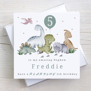 May include: A white card with a green dinosaur theme. The card says "to my amazing Nephew Freddie have a ROARSOME 5th birthday". There are illustrations of dinosaurs and a number 5 in a circle.