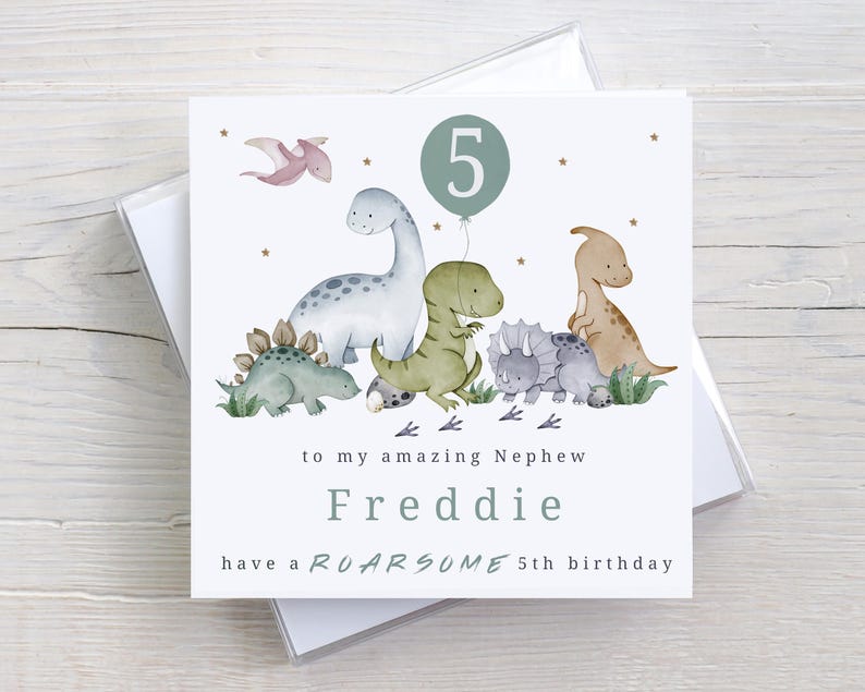 May include: A white card with a green dinosaur theme. The card says "to my amazing Nephew Freddie have a ROARSOME 5th birthday". There are illustrations of dinosaurs and a number 5 in a circle.