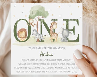 May include: A green and gold card with the word "ONE" in large letters. The letters are decorated with jungle animals, including a lion, zebra, giraffe, and elephant. The card reads "To our very special grandson Archie. Today's a very special day. It has come round very fast. We can't believe you're turning one. Oh how the year has passed. We've watched you learn and laugh and smile and marvelled as you grew. We can't believe you've been here a year. Happy first birthday to you!"