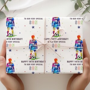May include: White wrapping paper with a colorful soccer player design. The paper has the text "Happy 14th Birthday! To our very special son" repeated on each side.