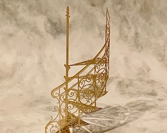 Op de afbeelding: Een goudkleurige metalen miniatuur wenteltrap met ingewikkelde filigraan krulpatronen op de treden en leuningen. De structuur bevat een centrale verticale steunpaal en een gebogen leuning met gedetailleerde decoratieve uitsparingen.