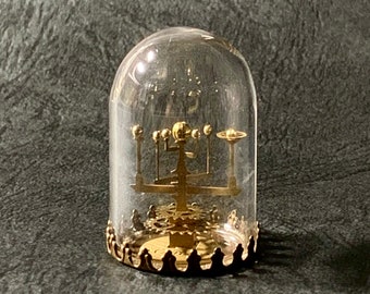 May include: A gold-colored metal model of a solar system under a glass dome with a gold-colored base.