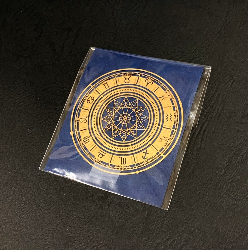 Op de afbeelding: Een gouden metalen dierenriemwiel met Romeinse cijfers en astrologische symbolen op een blauwe achtergrond.
