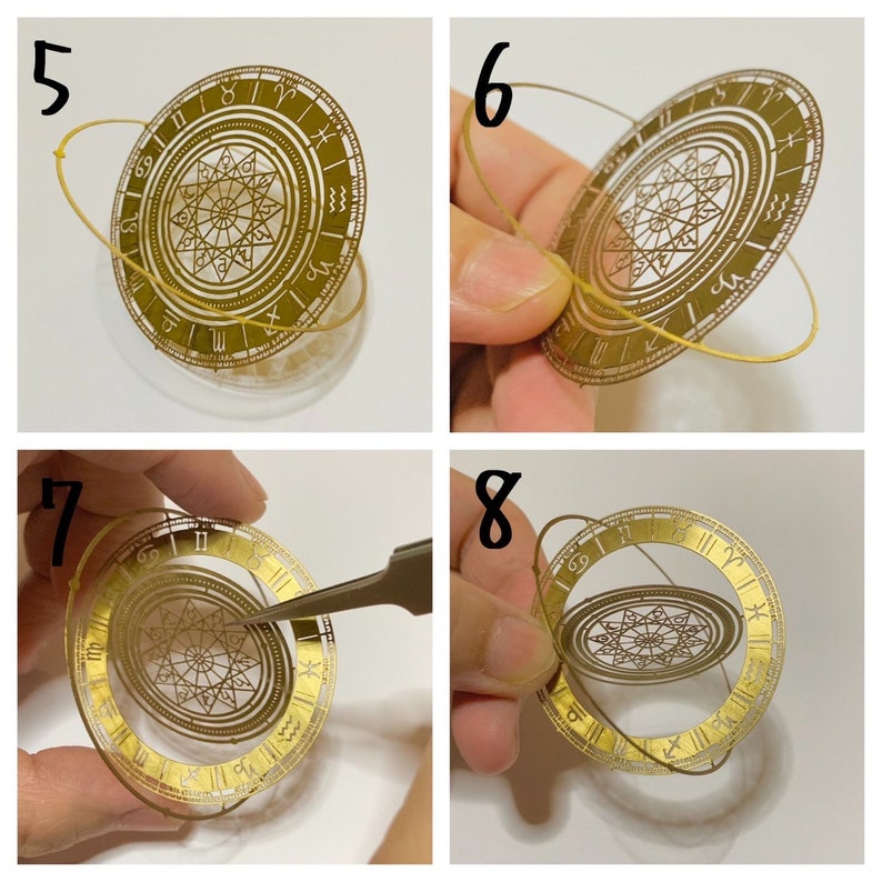 Op de afbeelding: Een gouden metalen ornament met een cirkelvormig ontwerp met Romeinse cijfers en astrologische symbolen. Het ornament wordt opgehangen met een dun, doorzichtig elastiek. Het ornament wordt in verschillende stadia van montage getoond.