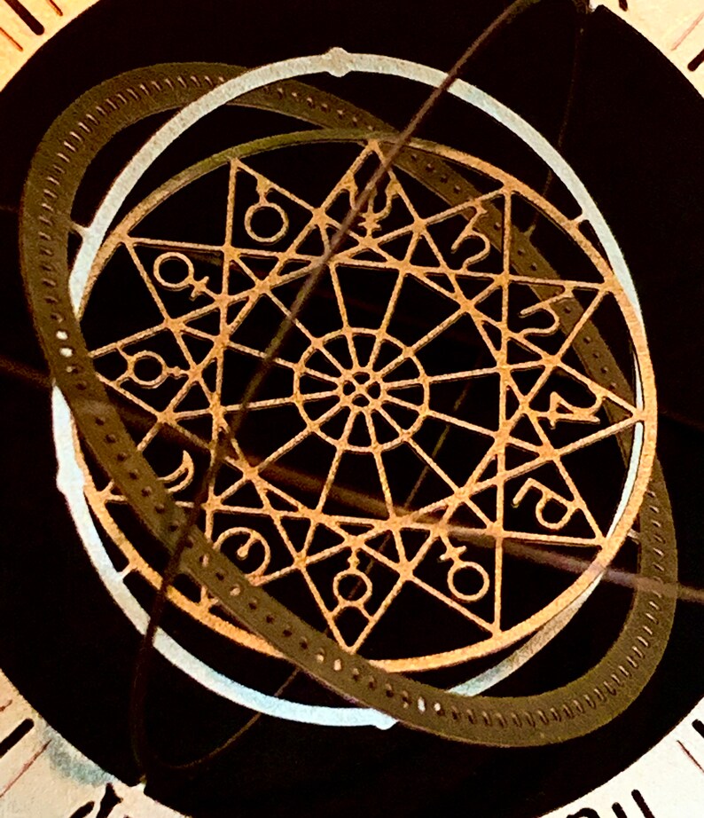 Op de afbeelding: Een close-up van een decoratieve wijzerplaat met een ingewikkeld, goudkleurig ontwerp met een stervormig patroon en astrologische symbolen. De wijzerplaat is omgeven door een zwarte achtergrond.