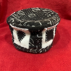 May include: A black and white patterned hat with a rounded crown and a short brim. The hat features a repeating pattern of white shapes on a black background, with white stitching details. The hat is likely handmade.