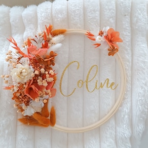 May include: A round wooden embroidery hoop with dried flowers and greenery in shades of orange and white. The name "Coline" is written in gold glitter lettering on the hoop.