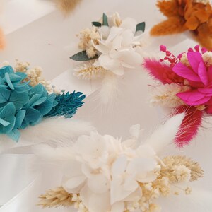 May include: Assortment of dried flower arrangements in various colors, including white, pink, blue, and orange. The arrangements feature dried flowers, grasses, and other botanical elements.