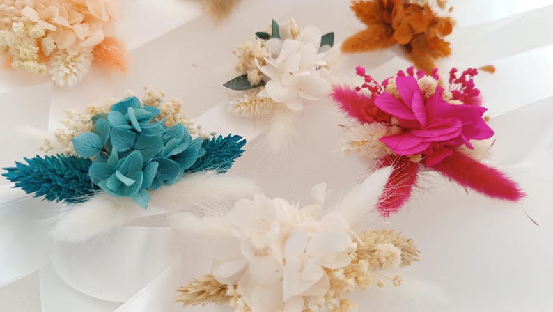 May include: Assortment of dried flower arrangements in various colors, including white, pink, blue, and orange. The arrangements feature dried flowers, grasses, and other botanical elements.