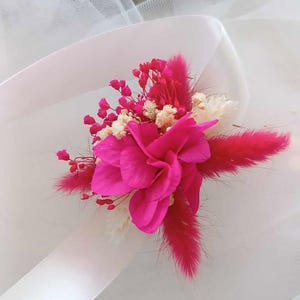 May include: A pink flower bouquet with white and pink dried flowers, and a pink feather, tied with a white ribbon.