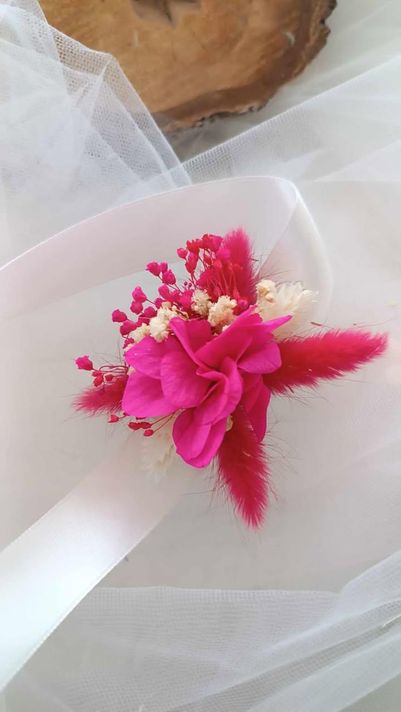 May include: A pink flower bouquet with white and pink dried flowers, and a pink feather, tied with a white ribbon.