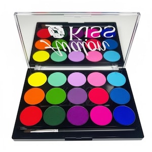 Puede incluir: Una paleta de sombras de ojos negra con 15 colores circulares vibrantes, incluyendo amarillo, naranja, rojo, verde, morado, rosa y azul. La paleta incluye un pincel y un espejo con el texto "Kiss Magic".