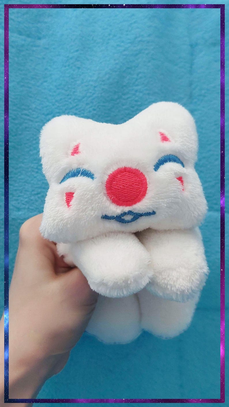 May include: A white plush toy with a smiling face, featuring a red circle nose, blue eyebrows, and small pink accents. The toy is held against a blue background with a purple and blue border.