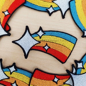 Pode incluir: Um conjunto de cinco patches para passar a ferro com um design de arco-íris. Cada patch tem a forma de uma estrela cadente com estrelas brancas.