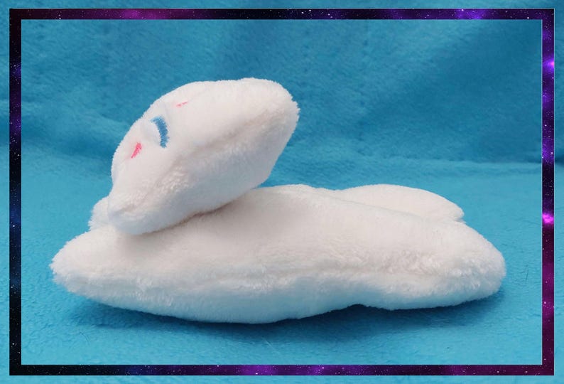 May include: A white plush cloud-shaped pillow with a small face embroidered with blue and pink details. The pillow is on a blue background and framed with a purple and black border.