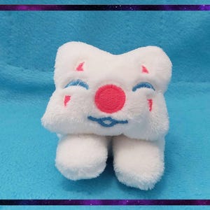 May include: A white plush toy with a smiling face, featuring a pink nose, blue eyes, and red accents. The toy has a star-like shape and two small feet. The background is a light blue fabric with a purple and black border.