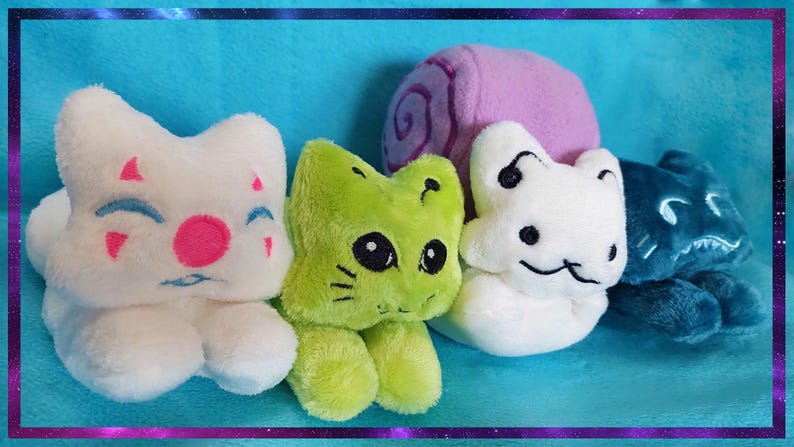 May include: A collection of plush cat toys in various colors. The toys include white, green, and blue cats, and a purple snail. The white cat has pink and blue facial details. The green cat has black eyes and whiskers.