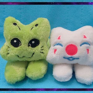 May include: Two plush toys: one green with black eyes and a smiling face, the other white with a red nose and blue accents. Both have a four-lobed shape and small legs. The background is a solid blue with a purple and black border.