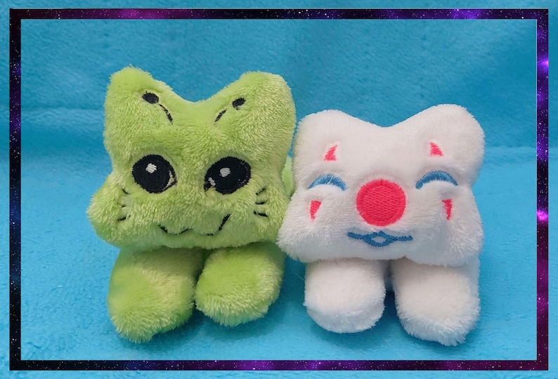 May include: Two plush toys: one green with black eyes and a smiling face, the other white with a red nose and blue accents. Both have a four-lobed shape and small legs. The background is a solid blue with a purple and black border.