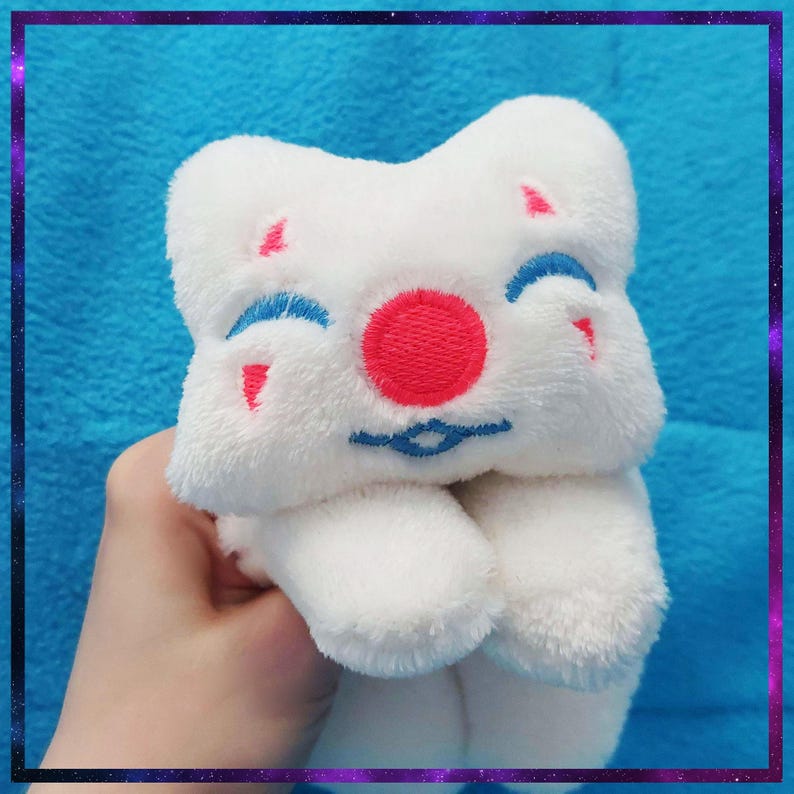 May include: A white plush toy with a smiling face, featuring a red nose, blue eyes, and pink accents. The toy has a soft, fluffy texture and a whimsical design, perfect for children or collectors.