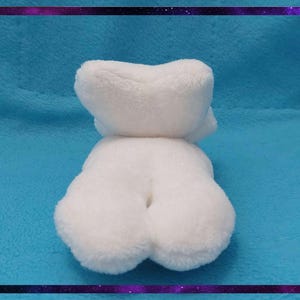 May include: A white plush toy in the shape of a bear, lying on a blue surface. The bear has a fluffy texture and a rounded shape. The image is framed with a purple and black border.