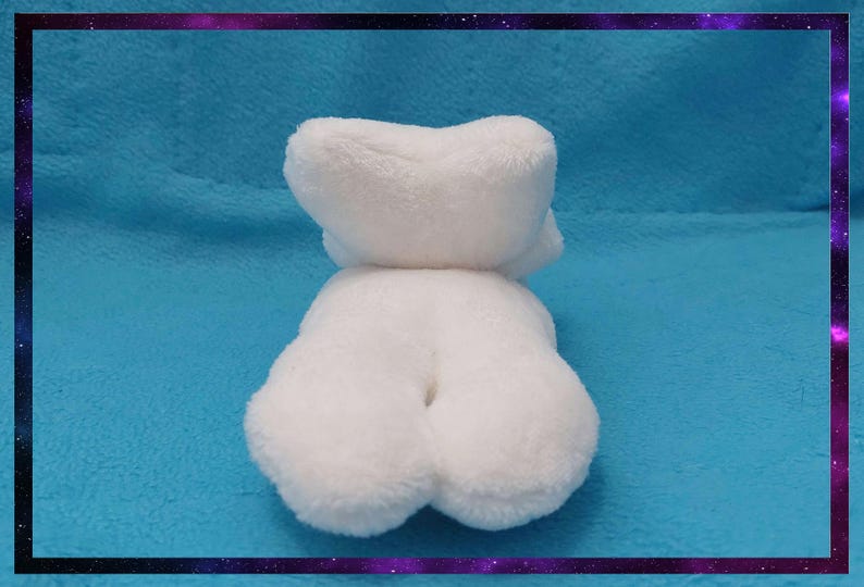 May include: A white plush toy in the shape of a bear, lying on a blue surface. The bear has a fluffy texture and a rounded shape. The image is framed with a purple and black border.