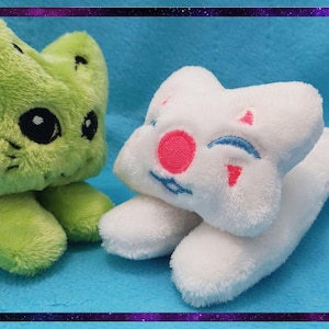 May include: Two plush toys: a green cat-like creature with black eyes and a white star-shaped character with a pink nose and blue smile. Both are on a blue surface, framed by a purple border.