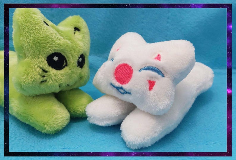 May include: Two plush toys: a green cat-like creature with black eyes and a white star-shaped character with a pink nose and blue smile. Both are on a blue surface, framed by a purple border.