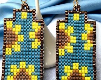 Op de afbeelding: Een paar kralen oorbellen met een rechthoekige vorm. De oorbellen hebben een patroon van gele en bruine vormen op een blauwe achtergrond, omlijst door een bruine rand. Goudkleurige haken maken het ontwerp compleet.