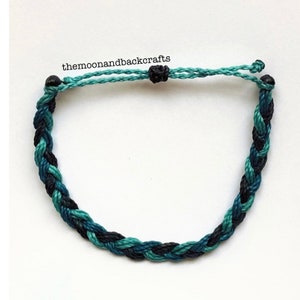 May include: A braided bracelet with black and blue cords. The bracelet has black beads at each end and is tied with a knot.