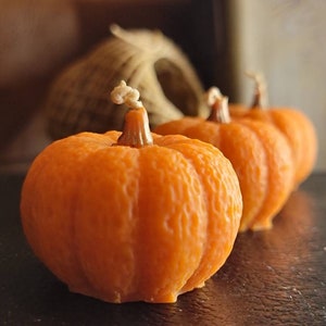 Peut inclure: Trois petites bougies en forme de citrouille orange sur une surface noire. Les bougies ont une surface texturée et sont allumées.