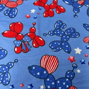 May include: A light blue fabric featuring a repeating pattern of balloon dogs in red, white, and blue. The balloon dogs are decorated with stars and stripes, and surrounded by star shapes.