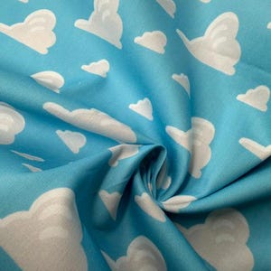 May include: Close-up of a blue fabric with a repeating pattern of white cartoon clouds. The clouds vary in size and shape, creating a whimsical, sky-like design. The fabric is slightly wrinkled, adding texture to the image.